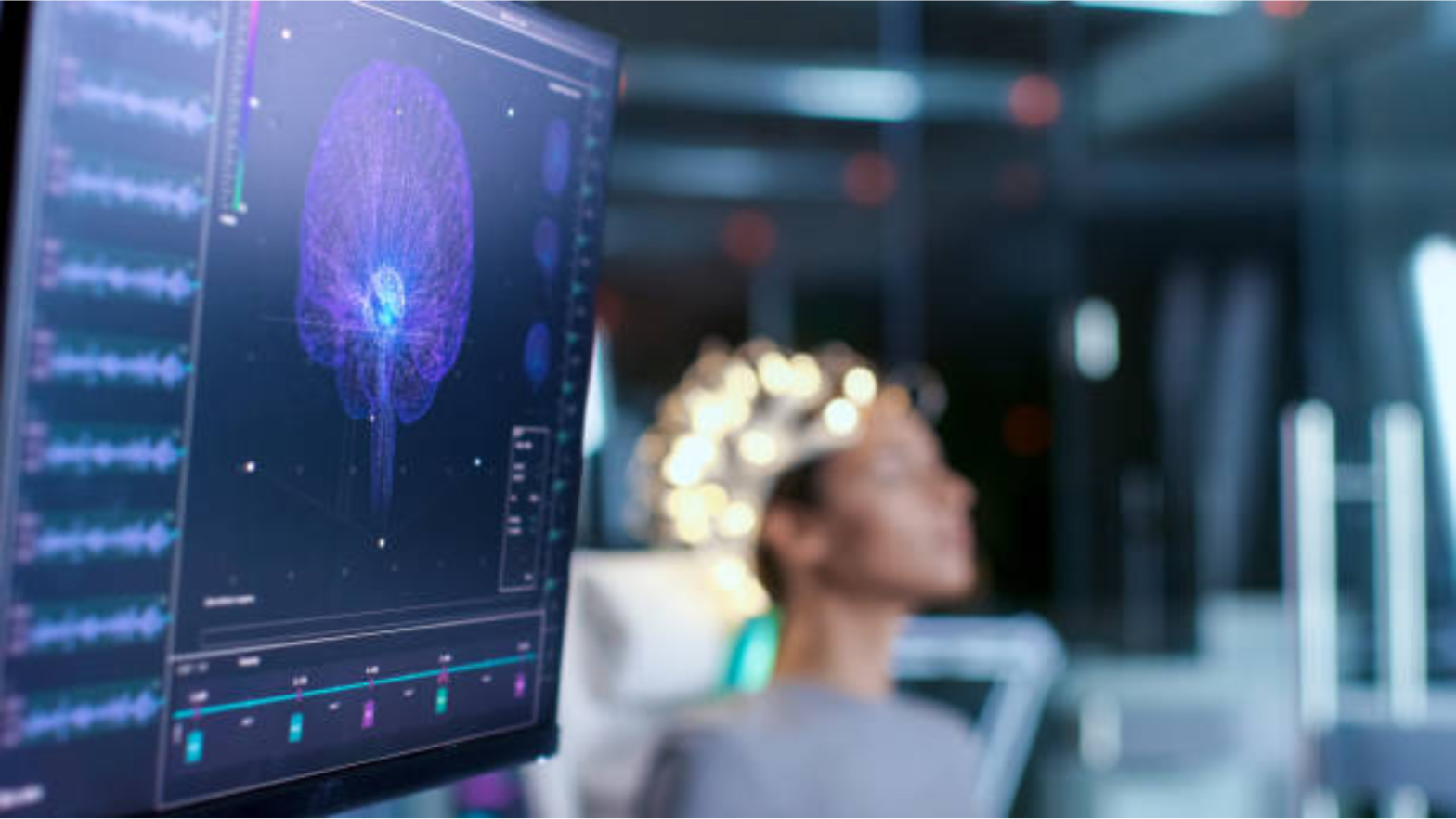Image shows close up of scan of a brain. In the background the person is having their brain scanned.